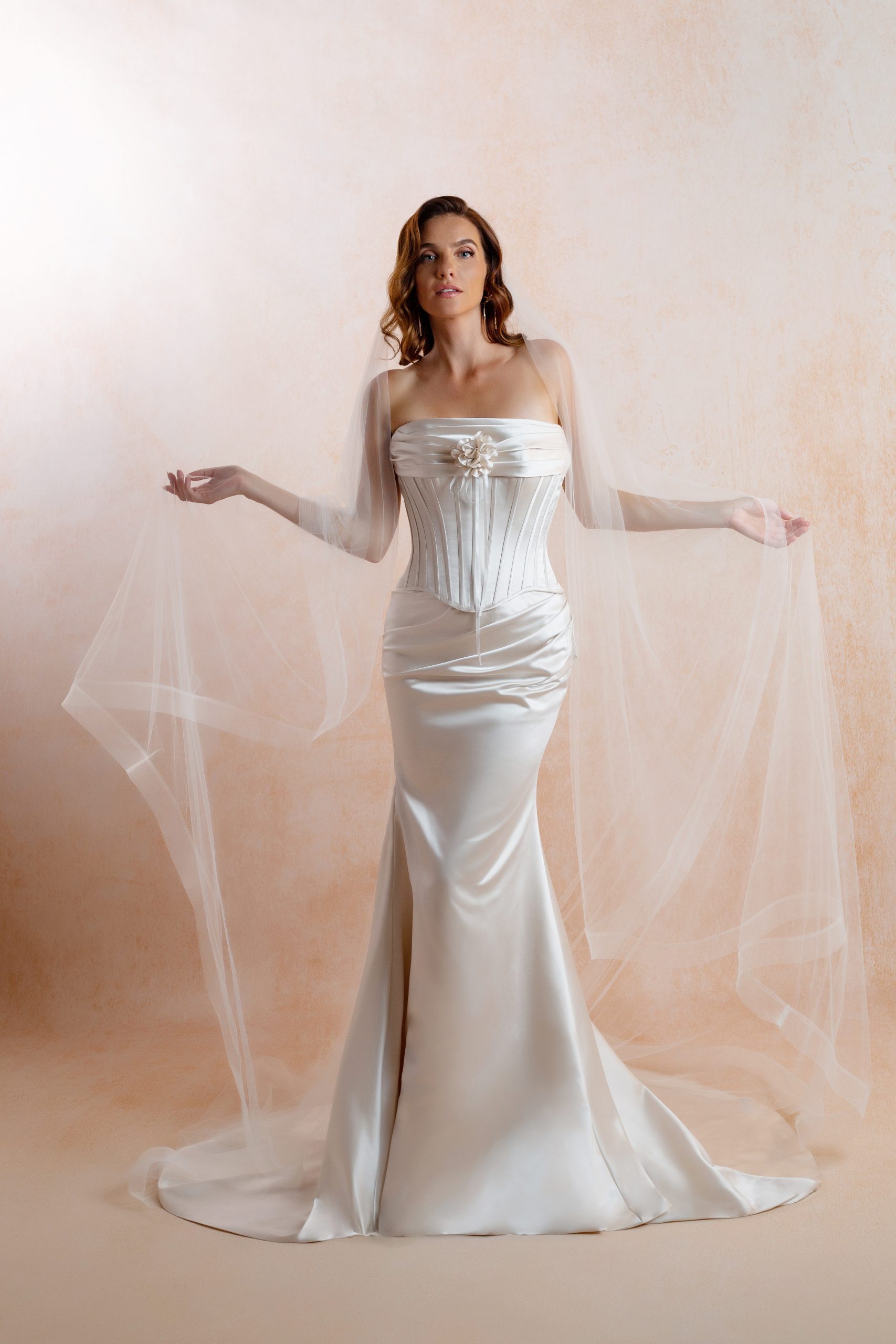 Bride wearing an ivory satin wedding dress with a structured corset bodice, draped strapless neckline, floral detail and fitted floor-length skirt.