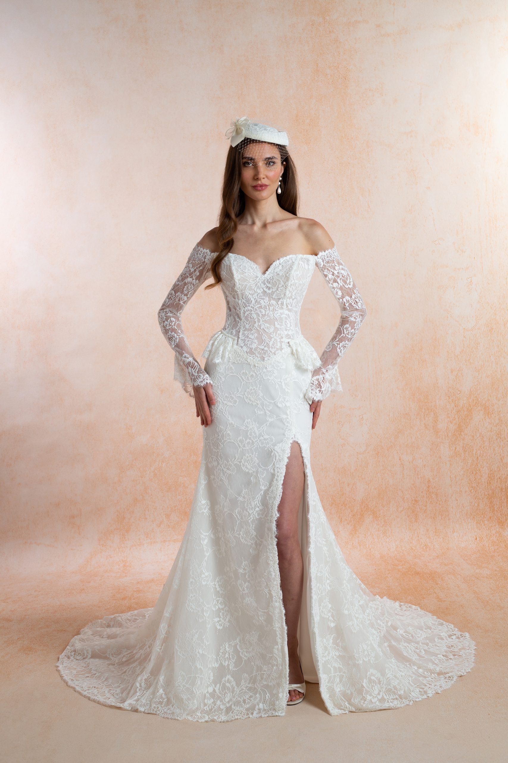 Bride wearing an ivory lace wedding dress with a structured corset bodice, long sheer lace sleeves, fitted skirt, front slit and sweeping train.