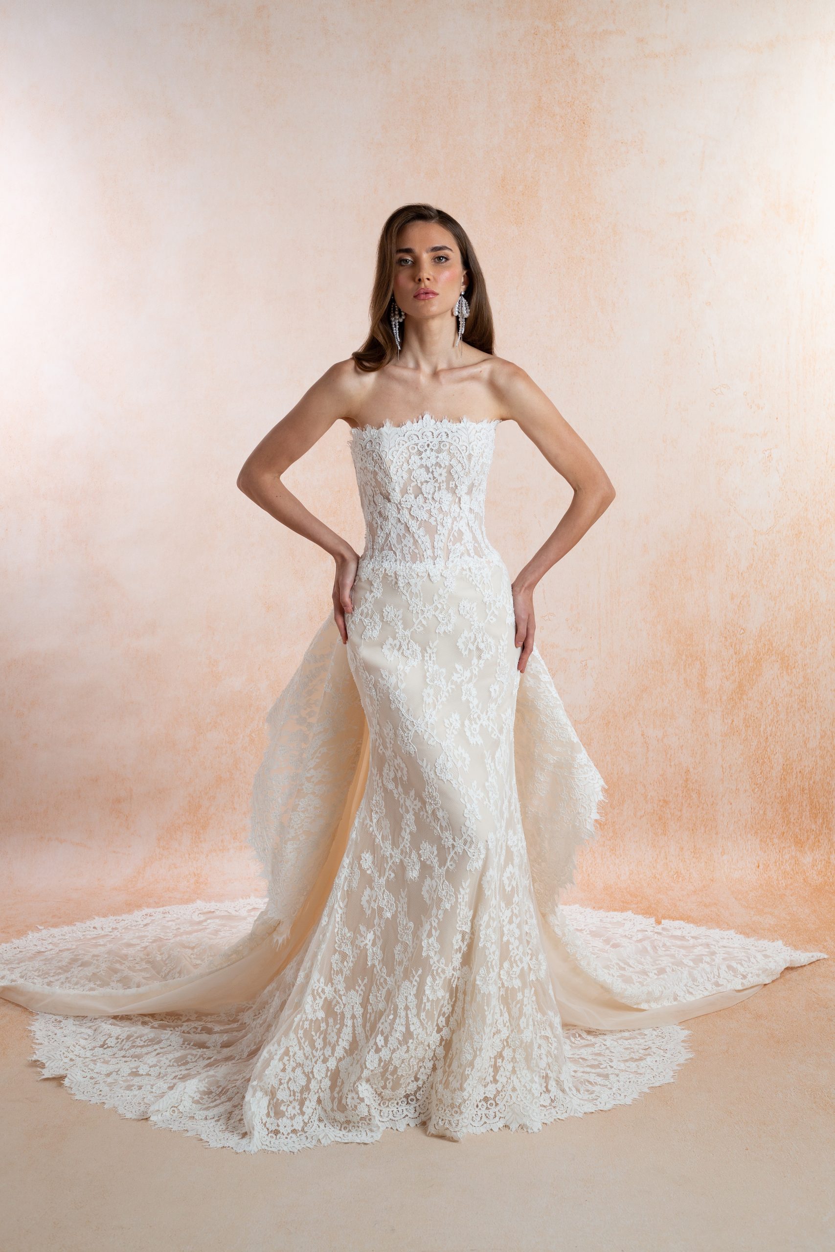 Model wearing a strapless floral lace fit-and-flare wedding dress with a sheer corset bodice and a sweeping lace train.