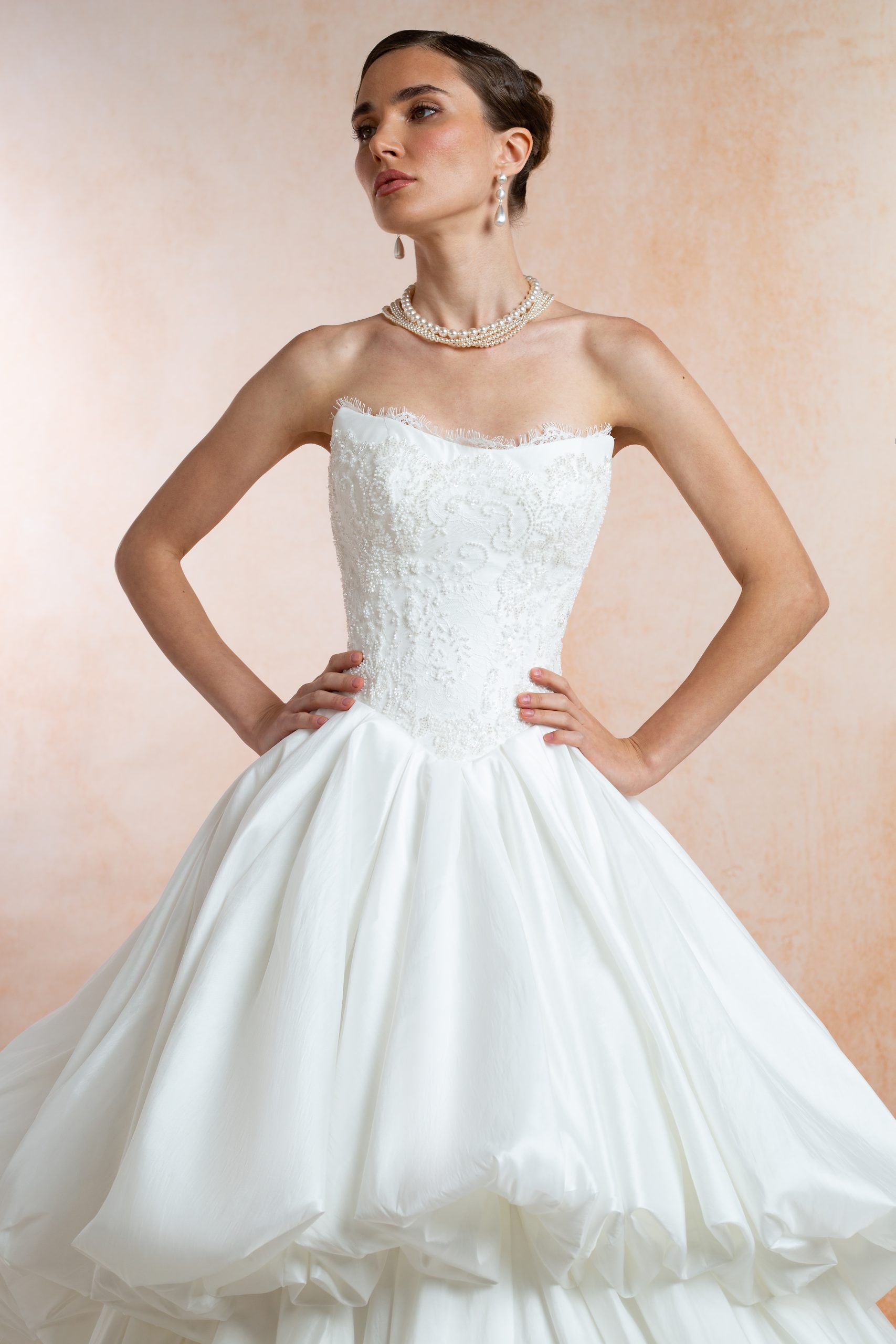 Bride wearing an ivory lace wedding dress with a structured corset bodice, long sheer lace sleeves, fitted skirt, front slit and sweeping train.