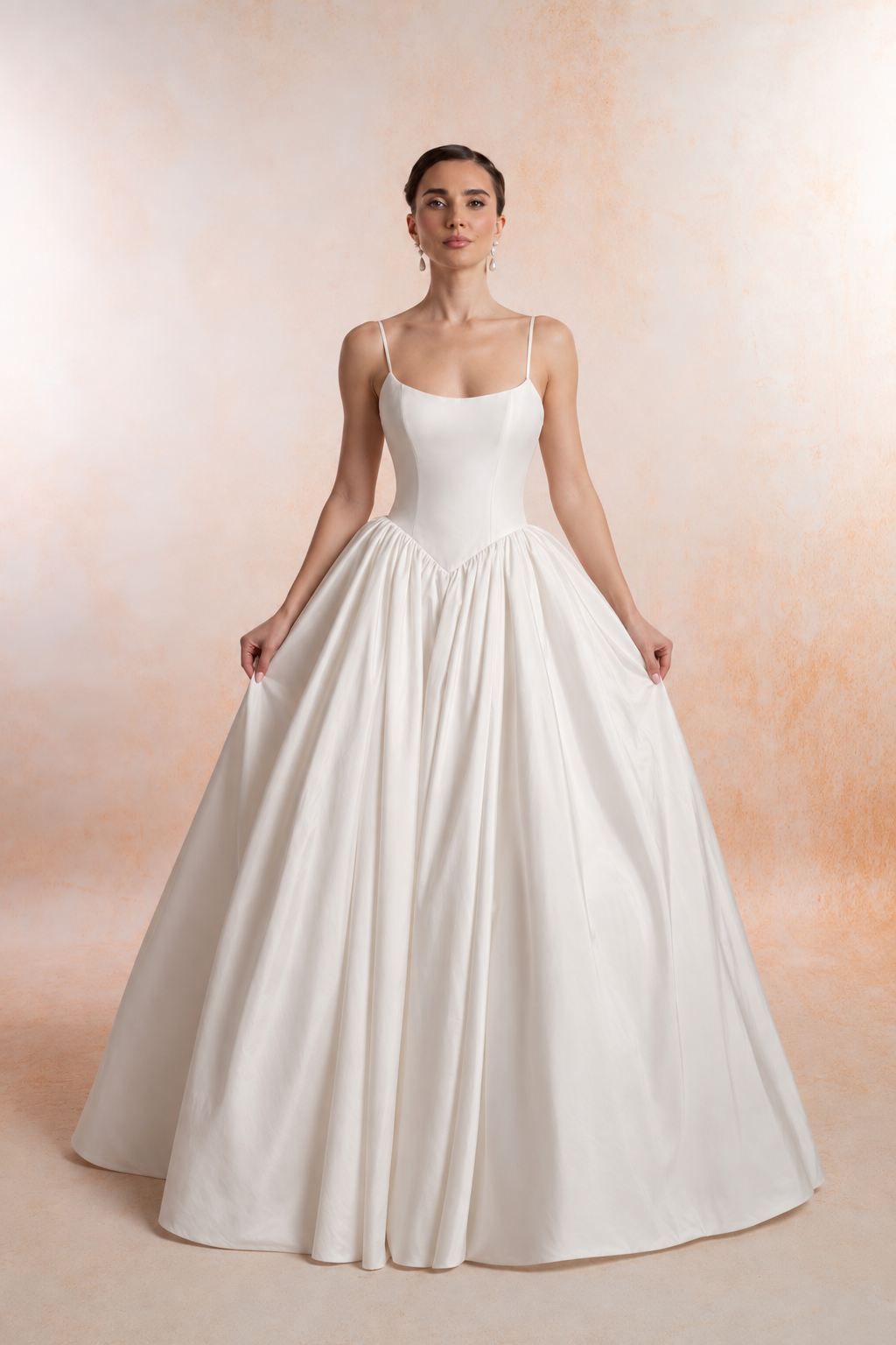 An ball gown wedding dress with a scoop neckline, delicate spaghetti straps and a structured bodice. The pointed V waist opens into a full, softly gathered skirt.