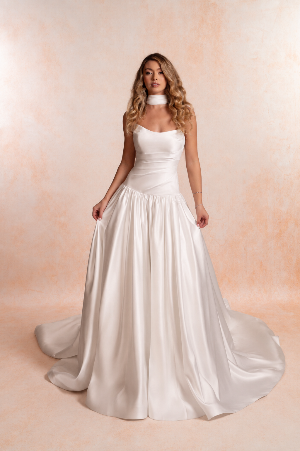 Model wearing a strapless satin wedding dress with a softly scooped neckline, fitted elongated bodice, dropped waist and full gathered A-line skirt with a sweeping train.