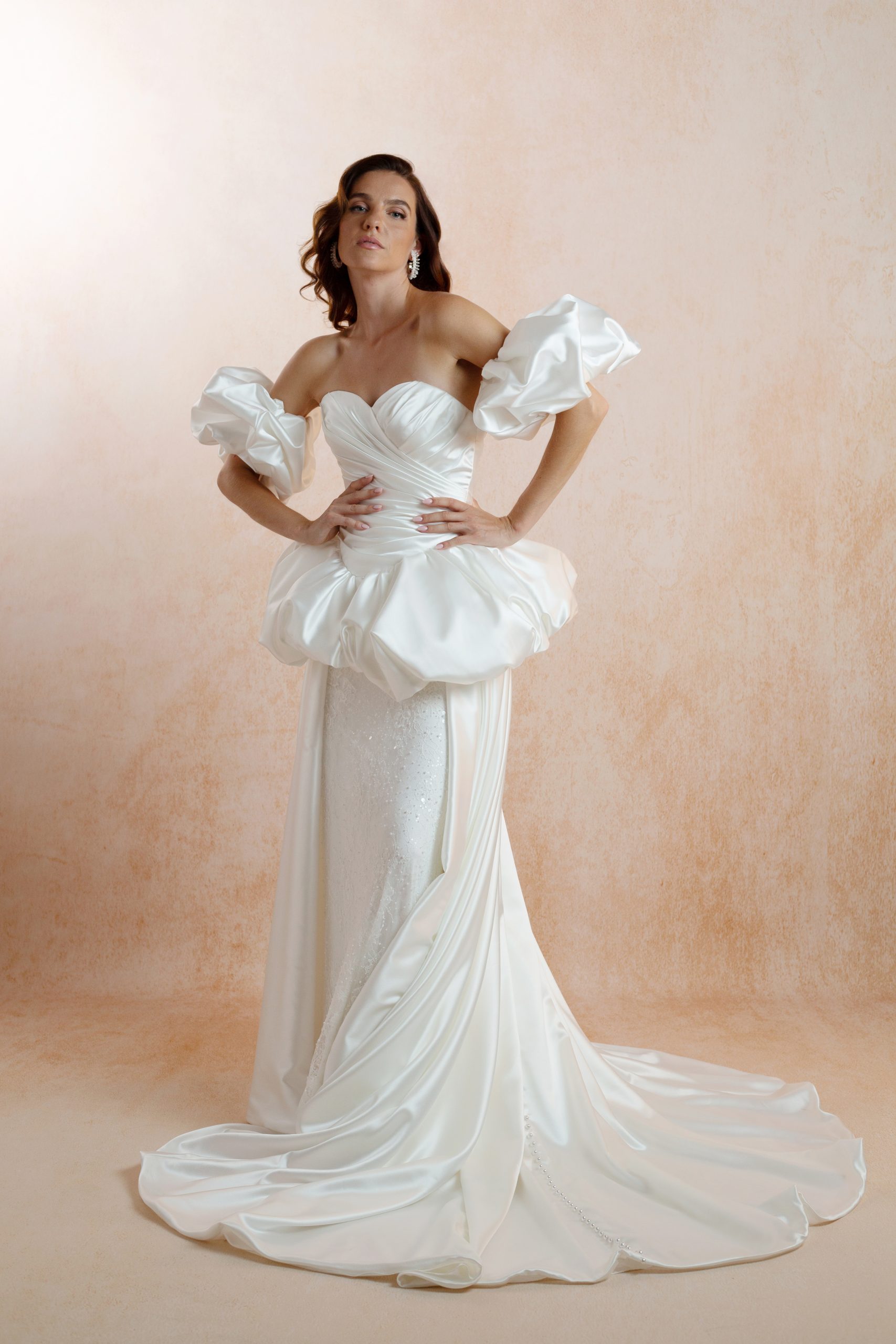 Model wearing a sweetheart wedding dress with a pleated satin corset, puff sleeves, beaded lace skirt and detachable bubble overskirt with a train.
